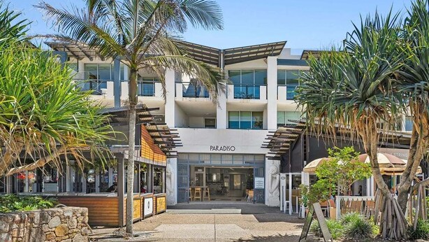 A modern building with a 'PARADISO' sign, featuring a central entrance, outdoor seating, and tropical landscaping. - Beachside Family Retreat - Paradiso 111 (Tweed)
