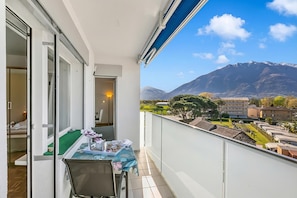 En balkon med et bord, stole og udsigt til bjerge og bygninger.