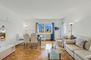 A modern living room with a glass coffee table, a sofa, a dining area with chairs, and a view of mountains through large windows. - Il Tenero Appartamento With Balcony and Parking (Tenero-Contra)