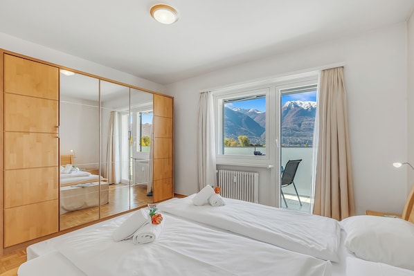 Une chambre avec un grand miroir, un lit, une fenêtre donnant sur les montagnes et une armoire en bois.