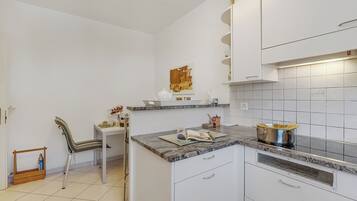 A kitchen with white cabinets, a marble countertop, and a small dining area with a chair and table.