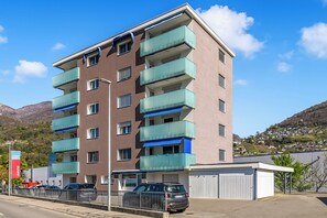 Un immeuble à plusieurs étages doté de balcons, d’un espace de stationnement et surplombant un paysage montagneux.