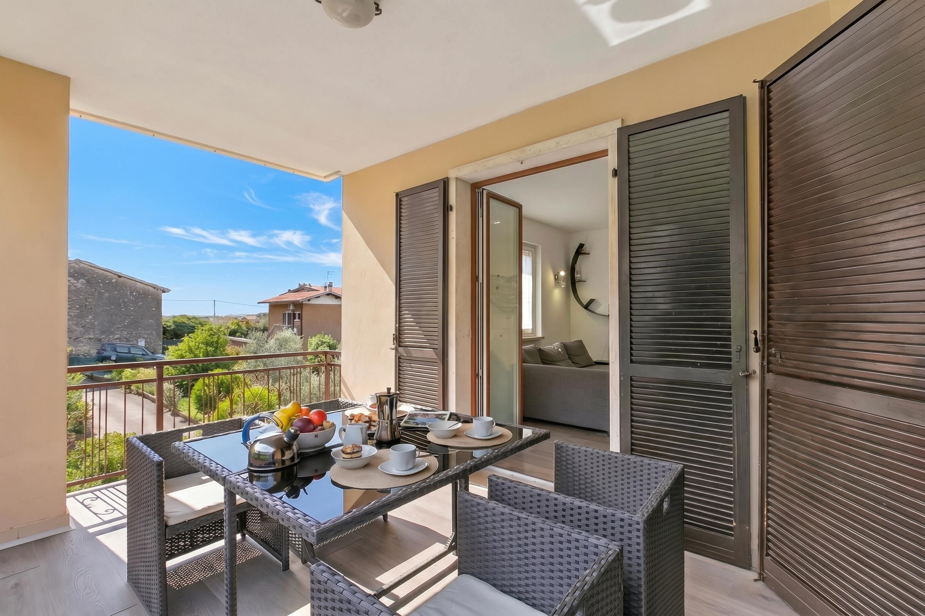 A balcony with a table set for breakfast, wicker chairs, and a view of the neighborhood.