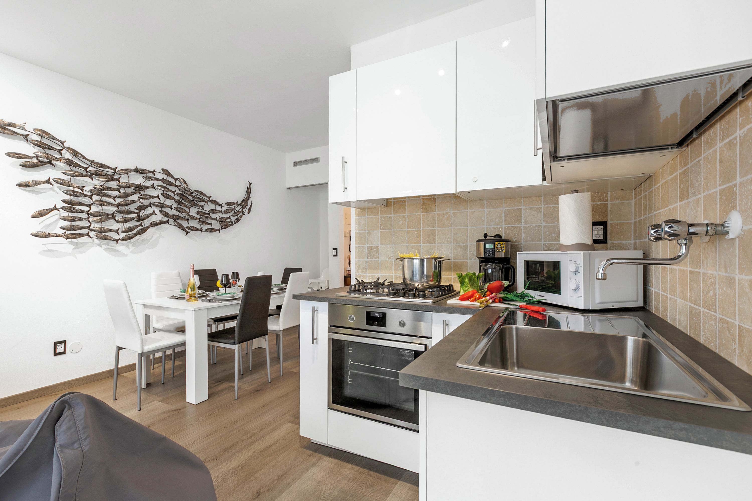 A modern kitchen with white cabinets, a stainless steel sink, and a decorative fish wall art.