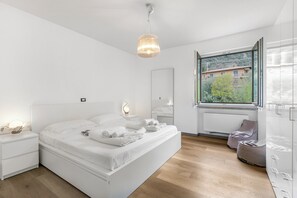 A modern bedroom with a large bed, bedside lamps, a window with a view, and a radiator. - Margherita Apartment - Lake and Mountain Views (Malcesine)