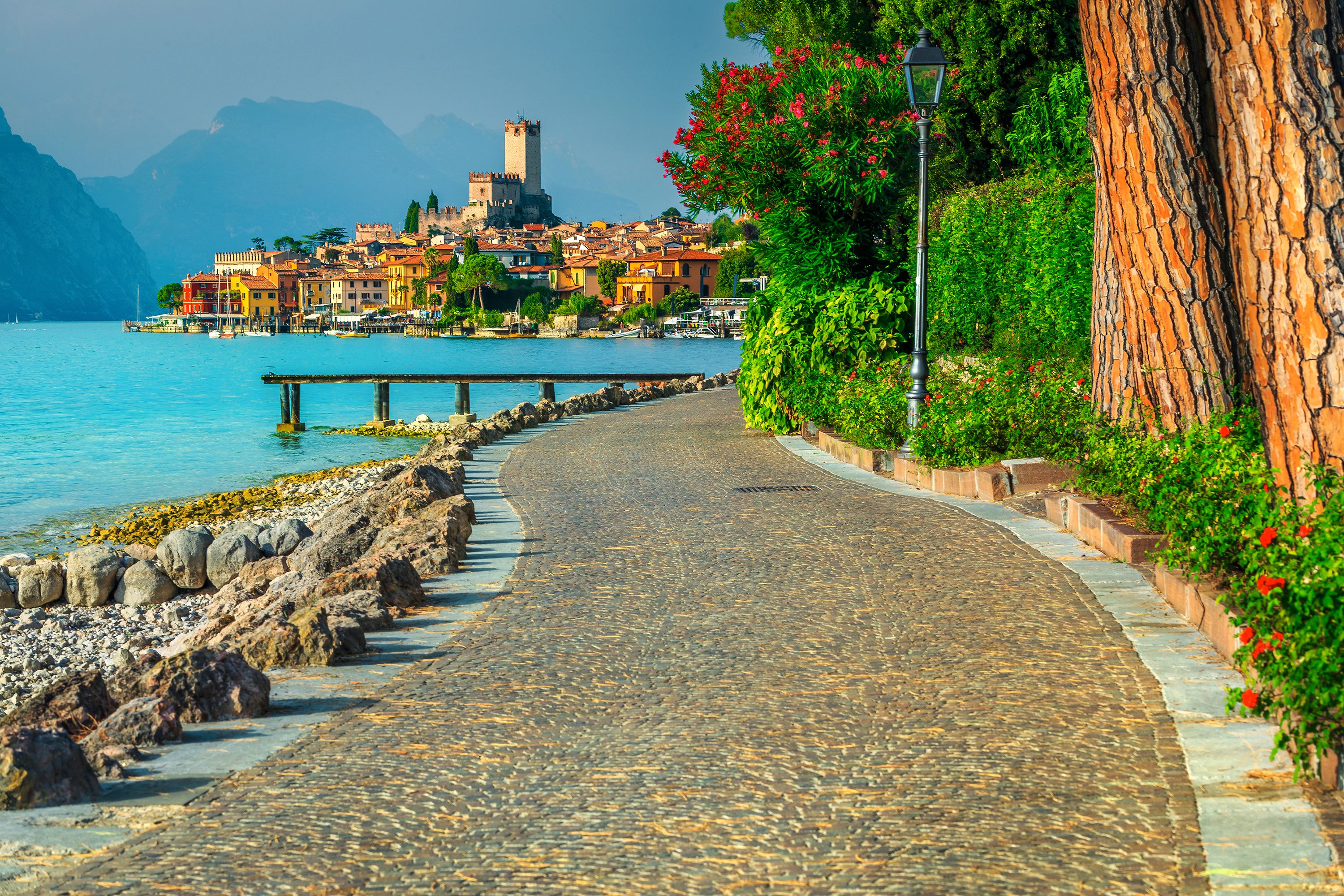 A cobblestone path leading to a coastal town with historic buildings, a prominent tower, and a rocky shoreline.