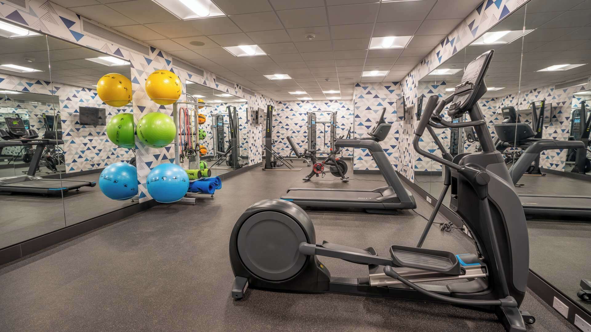 Een fitnessruimte met trainingsapparatuur, spiegels en een wand met een patroon.