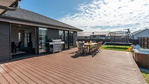 En moderne udendørs terrasse med grill, spisebord og jacuzzi.