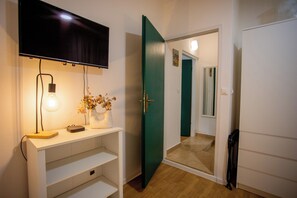 A room with a TV mounted on the wall, a desk with a lamp, a vase with flowers, and a green door leading to another room. - Casa Nora in centre of Vodnjan, Vodnjan, Croatia (Vodnjan)