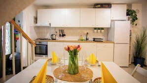 Een moderne keuken met witte kastjes, een fornuis en een spoelbak. Er staat een eettafel met gele placemats en een bloemenvaas.