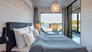 Une chambre avec un lit, un luminaire suspendu, une fenêtre et une vue sur un quai et des bâtiments.