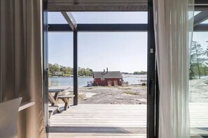 Puerta abierta que da a una terraza de madera con vistas a un lago y un edificio rojo.