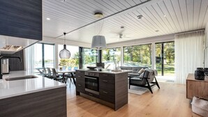 Une cuisine moderne dotée d’un îlot central, d’un coin repas avec des chaises et d’une grande fenêtre offrant une vue sur l’extérieur.