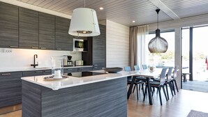Une cuisine moderne dotée d’un îlot central, de meubles de rangement aux couleurs sombres et d’un coin repas avec des chaises et une table.