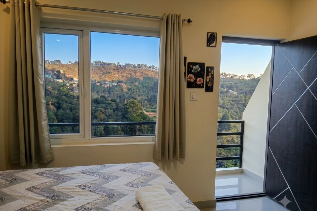 Un dormitorio con cama, ventana con cortinas, vistas a un área boscosa y una puerta que da a un balcón al aire libre.