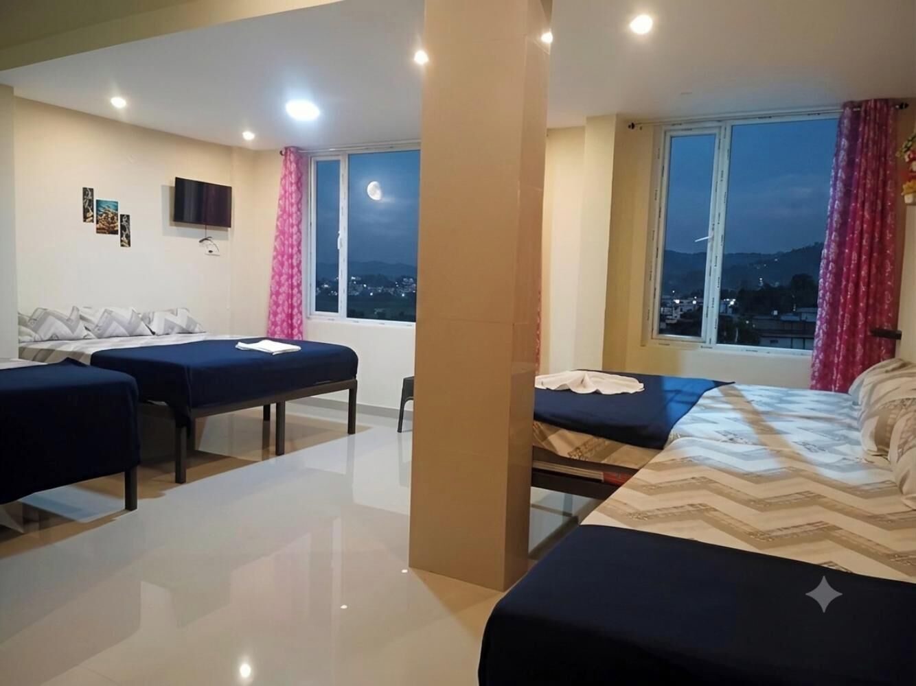 A hotel room with a bed, a desk, and a chair. There is a window with a view of the city.