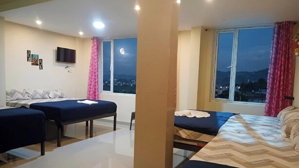 A hotel room with a bed, a desk, and a chair. There is a window with a view of the city. - Malabar Cottage - Panoramic Mountain View (Kodaikanal)