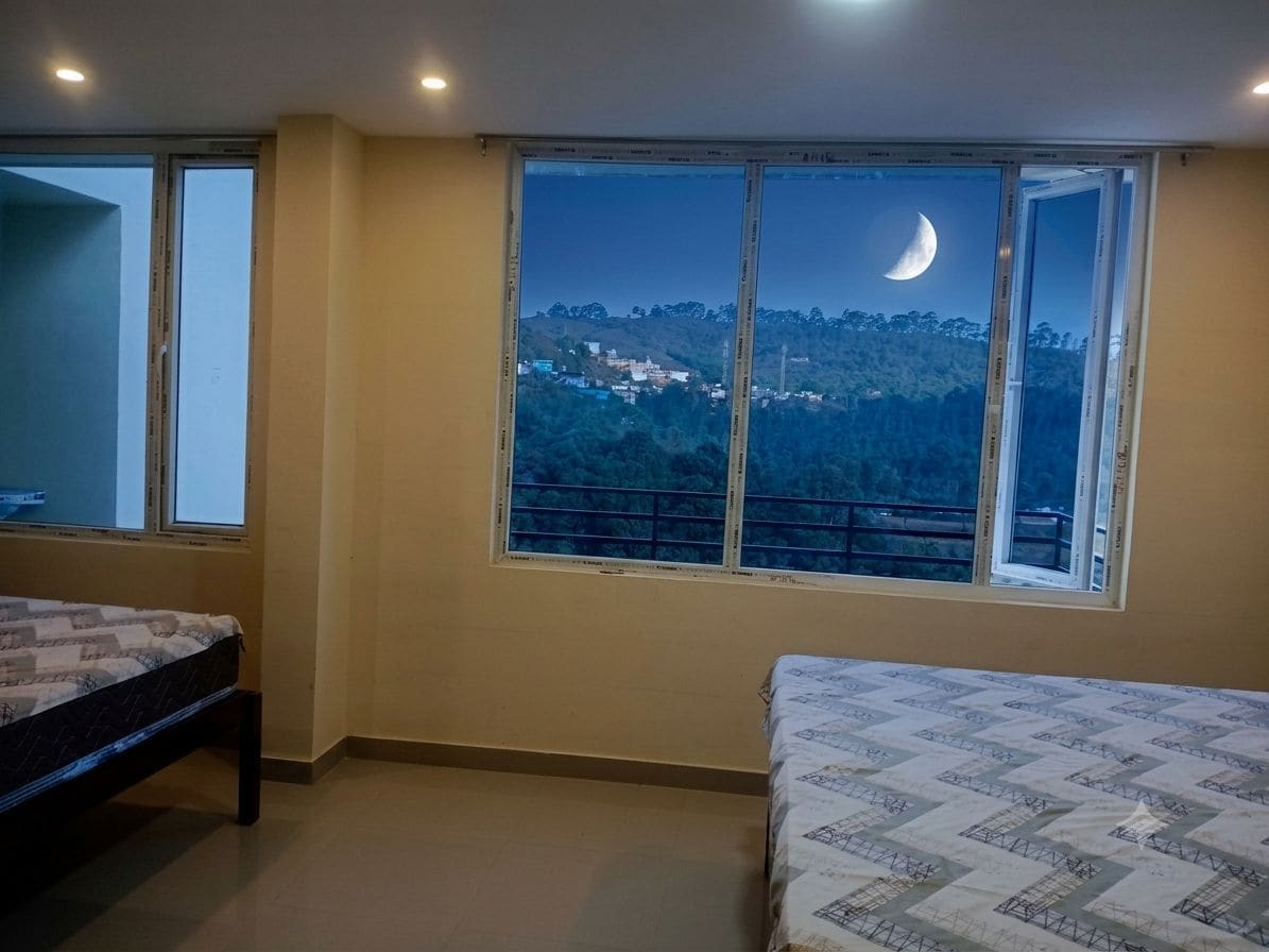 A bedroom with a large window, a bed, and a view of a hillside.
