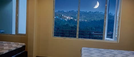 A bedroom with a large window, a bed, and a view of a hillside.