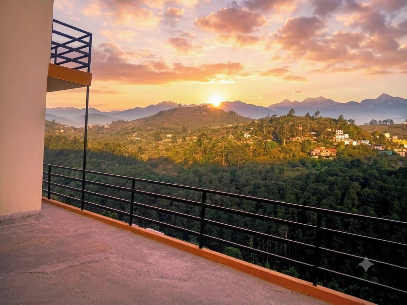 A balcony with a metal railing overlooking a mountainous landscape during sunset.