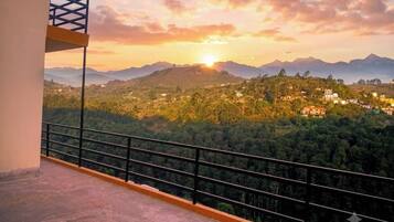 A balcony with a metal railing overlooking a mountainous landscape during sunset.