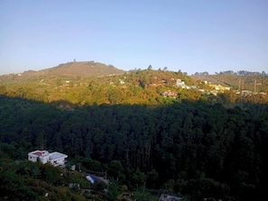 Un paisaje montañoso con edificios dispersos, un bosque denso y un cielo despejado.