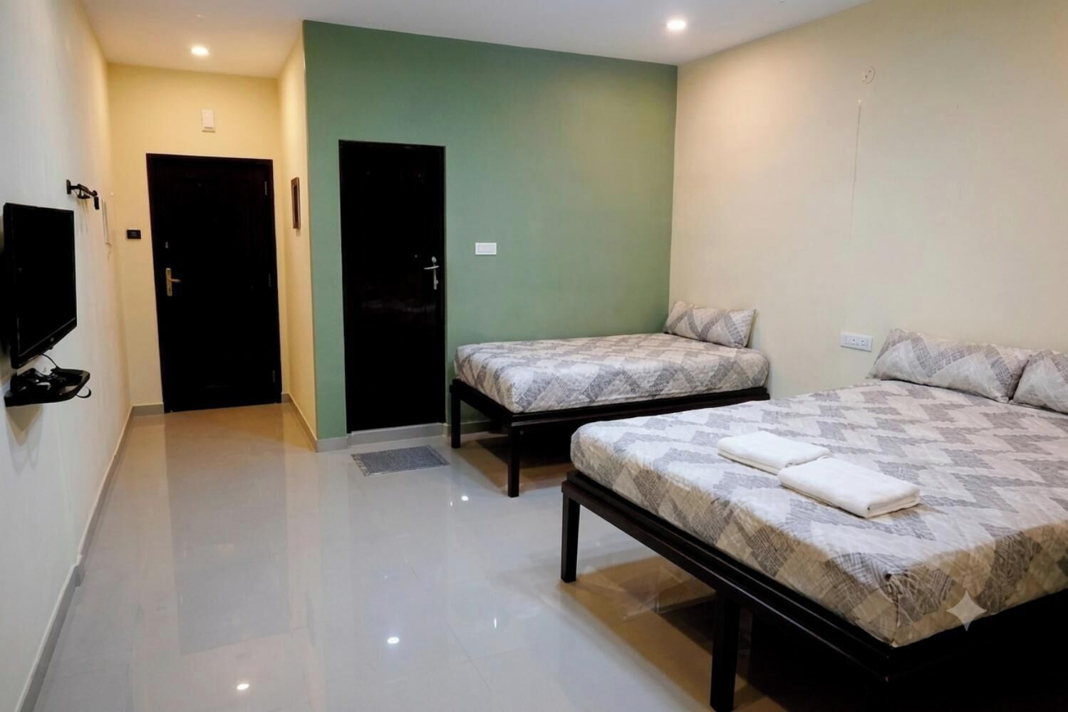 Habitación de hotel con dos camas, un televisor de pantalla plana montado en la pared y una puerta que da a otra habitación.