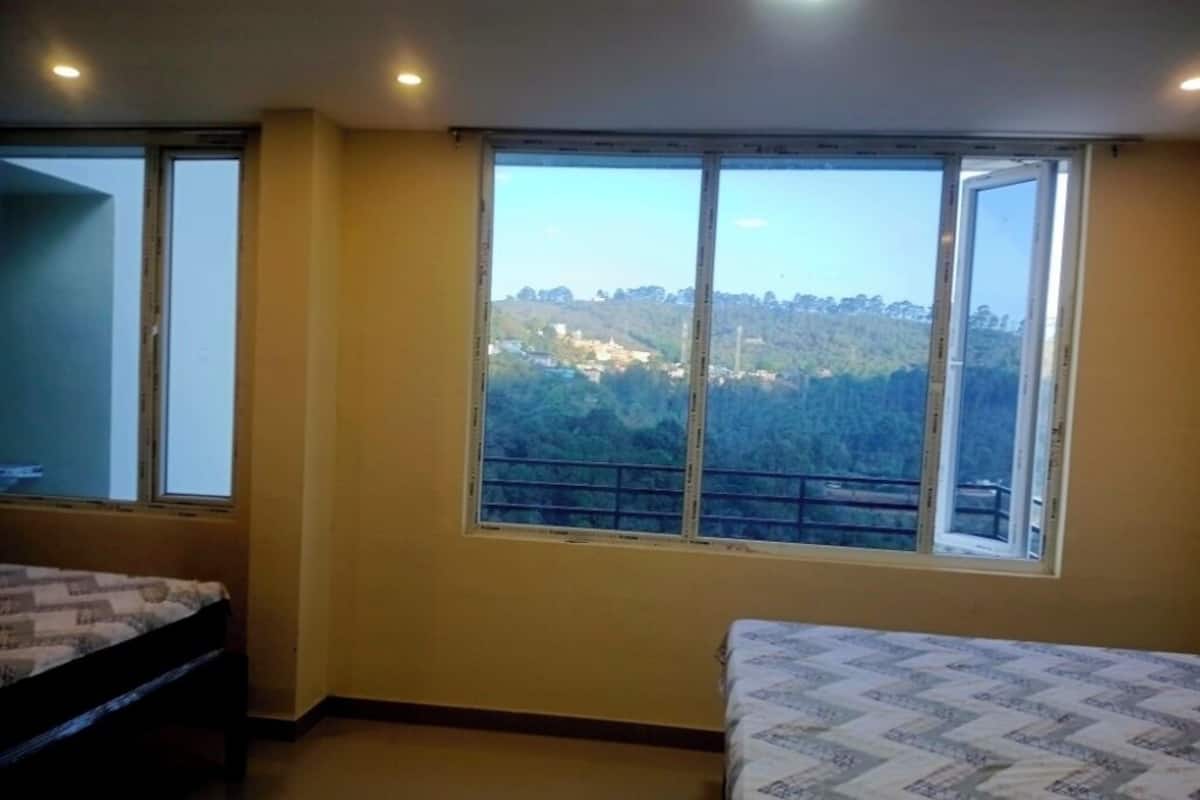 Una habitación con cama, ventana y vistas a un paisaje montañoso, e iluminación empotrada en el techo.