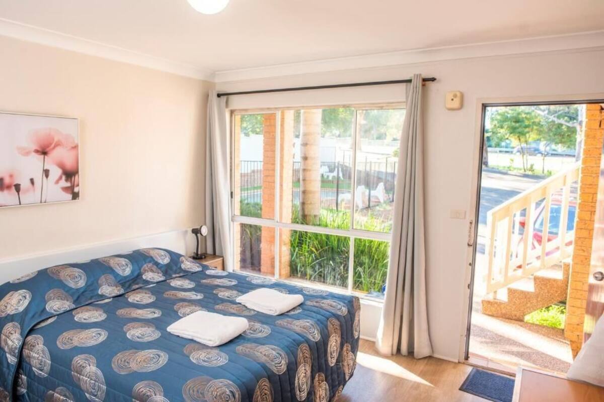 Une chambre à coucher avec un lit, une fenêtre avec des rideaux, une porte donnant sur l’extérieur et un tableau accroché au mur.