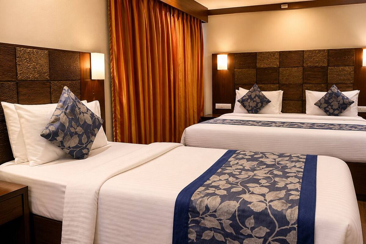 Habitación de hotel con dos camas, un ventanal con cortinas, una mesita de noche y una lámpara de pared.