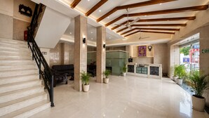 Un vestíbulo amplio con una escalera de mármol, un mostrador de recepción y un ventanal grande.