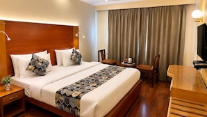 Habitación de hotel con una cama grande, cabecero de madera, mesitas de noche, un escritorio y un televisor.