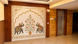 Un pasillo con un revestimiento decorativo que presenta elefantes y motivos florales, una puerta de madera y un aplique.