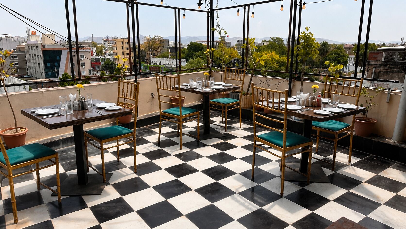 Terraço no telhado com piso xadrez, cadeiras de bambu com almofadas verdes e mesas preparadas para refeições.