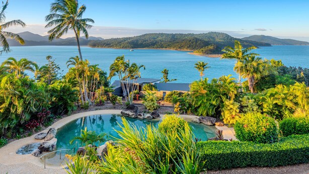 Une piscine entourée d’une végétation tropicale, avec vue sur une vaste étendue d’eau.