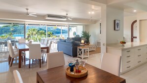 Un salon moderne avec un coin repas, de grandes fenêtres et une vue sur l’extérieur.