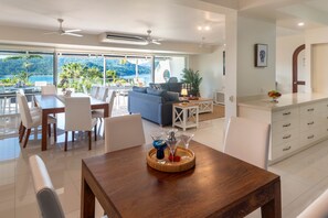 A modern living room with a dining area, large windows, and a view of the outdoors. - Bella Vista East 2 (Hamilton Island)