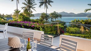 Une table avec des chaises et une bouteille de vin, offrant une vue panoramique sur un paysage agrémenté de palmiers et d’une étendue d’eau.
