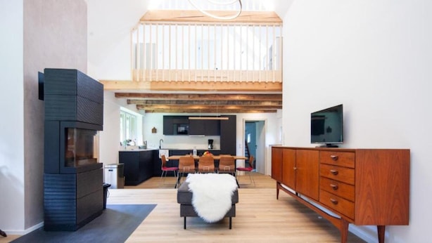 Un interior moderno con techo alto, comedor, sala de estar con sofá y televisor sobre un mueble de madera.