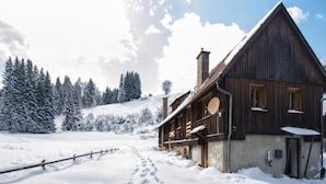 Una cabaña de madera con techo inclinado, rodeada de árboles cubiertos de nieve y un cielo despejado.