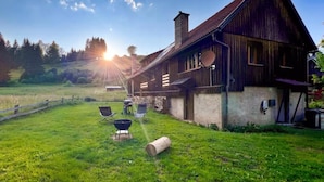 Una casa de madera rústica con techo inclinado, chimenea y patio vallado con mobiliario exterior.