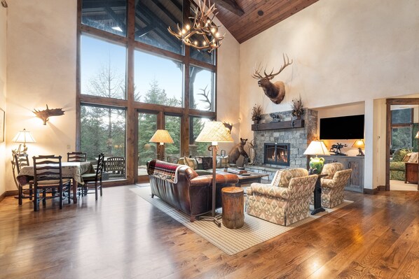 A spacious living room with a fireplace, large windows, and a mounted deer head.
