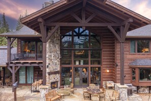 A log cabin with a stone fireplace, outdoor seating, and large windows.