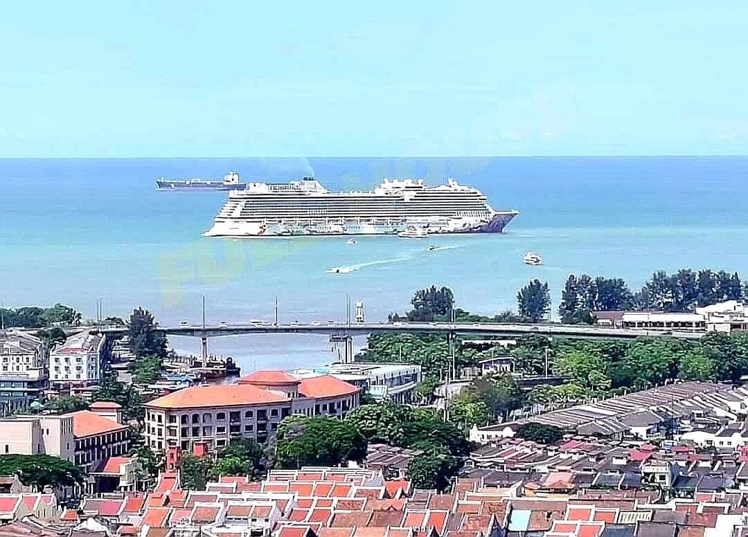 Un crucero amarrado cerca de una ciudad costera, con edificios y un puente al fondo.