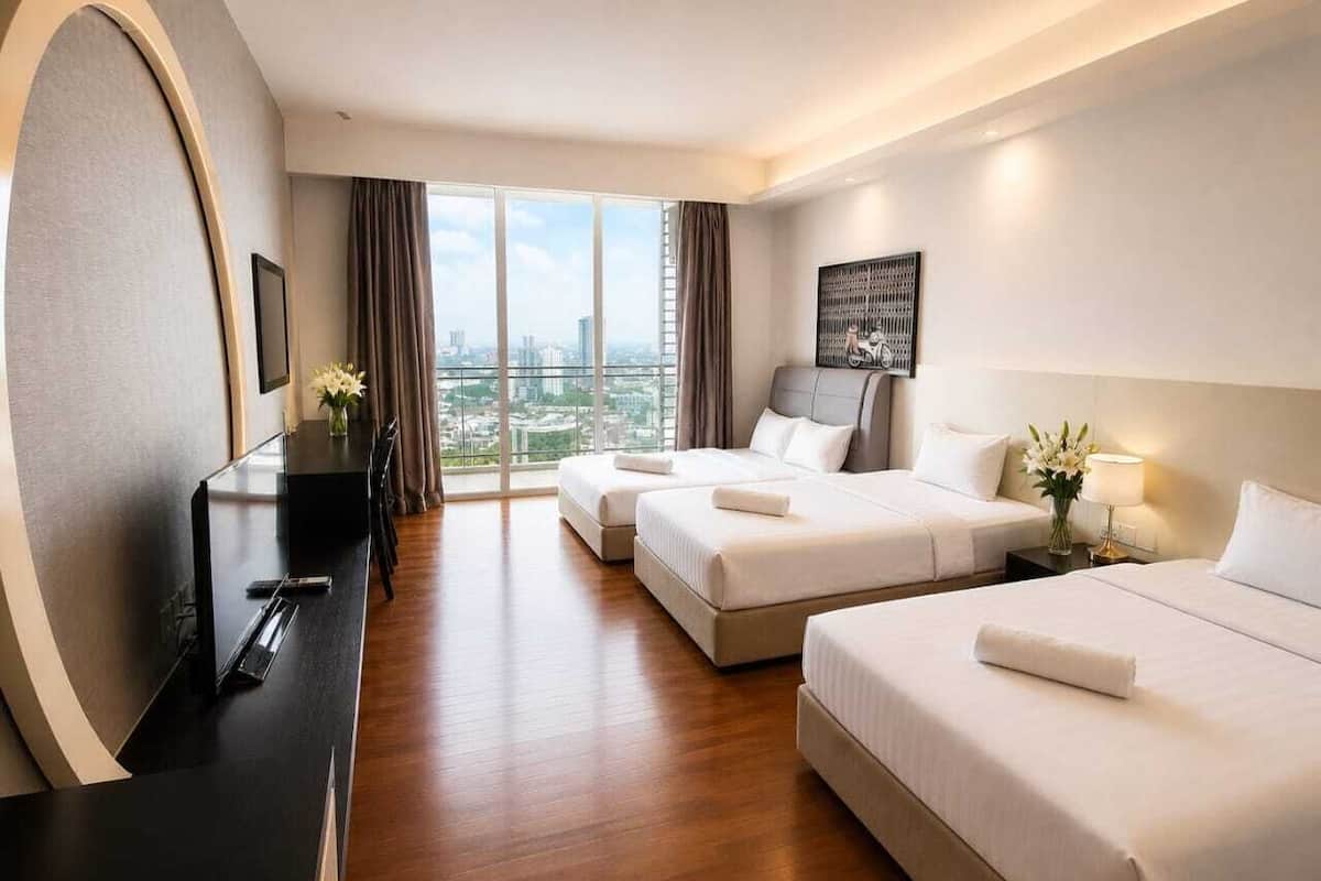 Ein Hotelzimmer mit zwei Betten, einem Schreibtisch, einem Stuhl, einem Fernseher, einem Fenster mit Vorhängen und Blick auf die Stadt.
