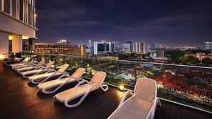 Um lounge no terraço com espreguiçadeiras e vista para a cidade ao entardecer.