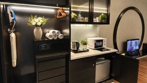 Uma cozinha compacta com micro-ondas, chaleira e um frigorífico pequeno.
