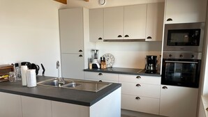 Een moderne keuken met een centraal eiland, roestvrijstalen apparatuur en witte kasten.