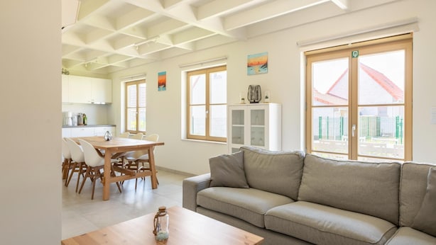 Een moderne woonkamer met een bank, een houten tafel en een eethoek met stoelen.
