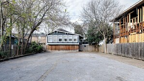 Un patio trasero residencial con una casa separada, una valla de madera y un camino de entrada pavimentado.
